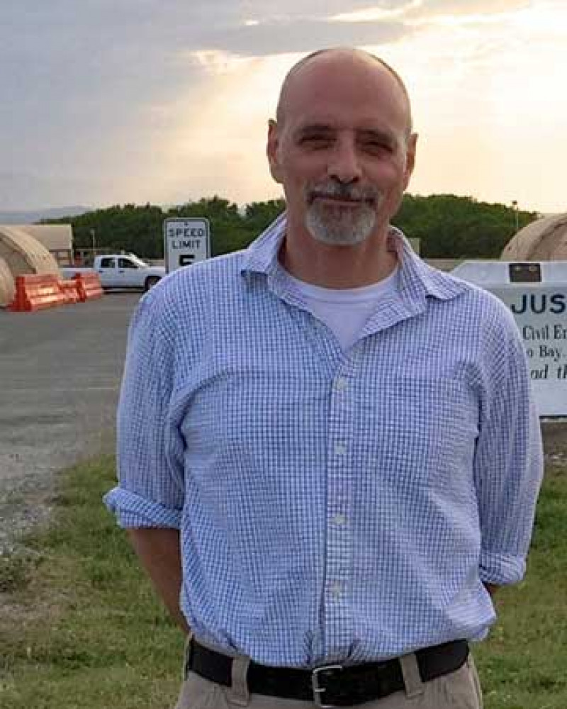 Man with a gray goatee wearing a checked shirt standing outdoors