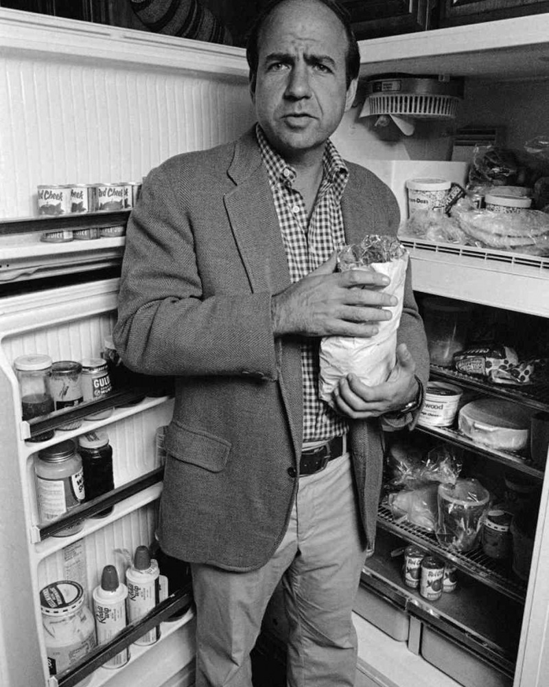 Calvin Trillin standing in front of a refrigerator in a black and white photograph