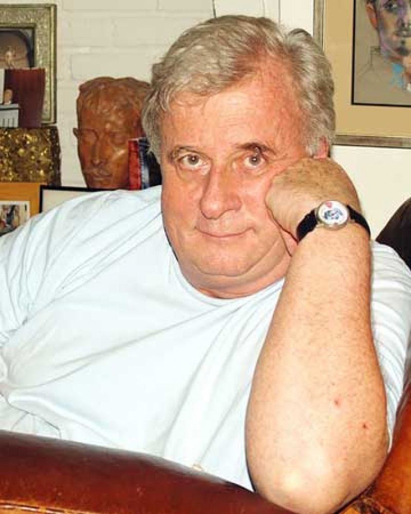 Photograph of a seated white-haired man in a white T-shirt