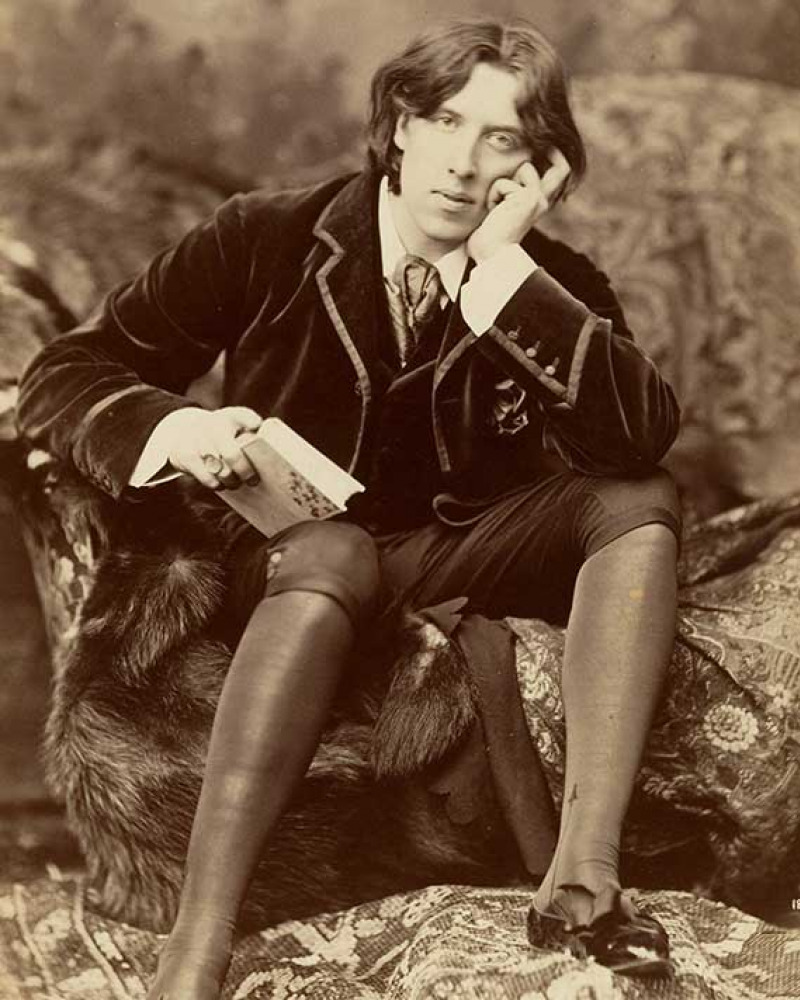 Sepia colored photo of Oscar Wilde sitting on a rock with a book in his hand