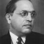 Profile of a man with wire-frame glasses and slicked-back hair looking right