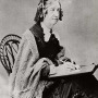 Woman wearing a shawl and writing while seated in a chair
