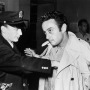 Black and white photo of Lenny Bruce being frisked by an officer