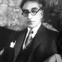 Black and white photograph of C. P. Cavafy wearing thick-rimmed black glasses. 