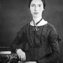 Black and white photograph of Emily Dickinson sitting next to a desk.