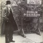 Flann O'Brien in an overcoat standing next to a Dublin Diversion sign