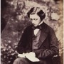 Sepia toned photograph of Lewis Carroll in a suit, reading a book