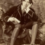 Sepia colored photo of Oscar Wilde sitting on a rock with a book in his hand